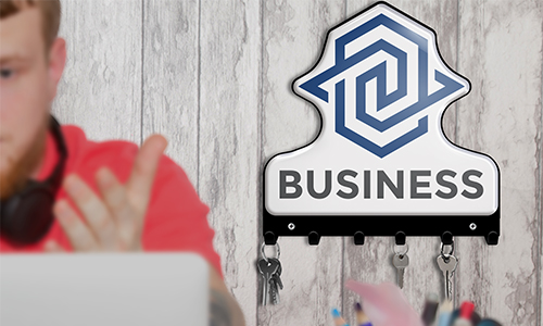 Persona con camiseta roja en laptop, auriculares al cuello; gancho de llaves con logotipo BUSINESS y llaves en la pared