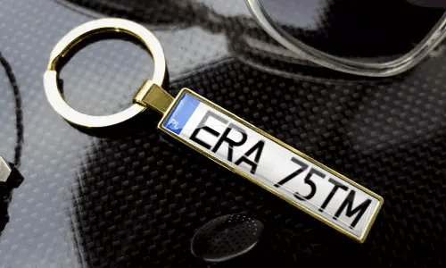Guldnyckelring med registreringsskylt visar graverad text i en polerad metallram