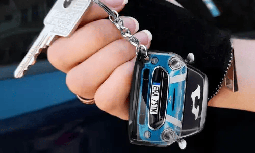 Hand hält einen Schlüsselanhänger in Form eines blauen Autos mit detaillierter Frontansicht
