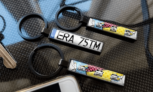 Portachiavi con targa in stile fumetto, esposti su una superficie con trama in carbonio e design colorati di auto