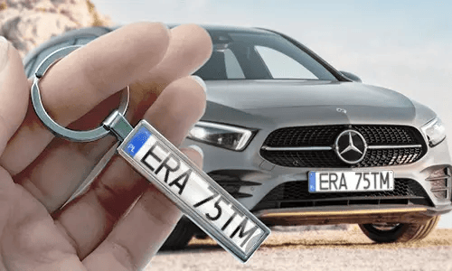 Sarjakuvatyylinen rekisterikilpien avaimenperä, kädessä pidettynä, taustalla vastaava autokilpi