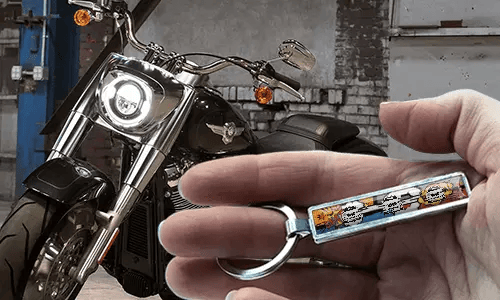 Sleutelhanger in stripstijl met kentekenplaat, vastgehouden in een hand, met een motor op de achtergrond