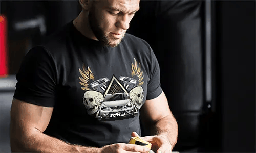 Schwarzes T-Shirt mit Grafik von Auto, Schädeln, Pistolen, goldenen Flügeln und sternförmigem Dreieckshintergrund