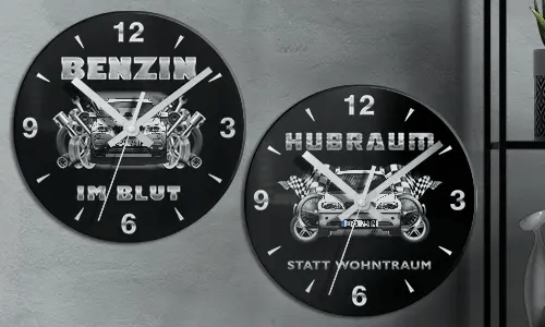 Zwei schwarze Wanduhren mit Autoillustrationen und deutschem Text: BENZIN IM BLUT und HUBRAUM STATT WOHNTRAUM